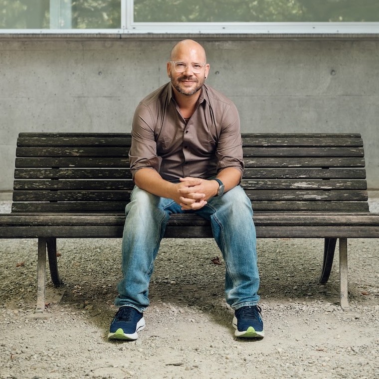Adrian Leemann sitting on a wooden bench in front of a concrete wall